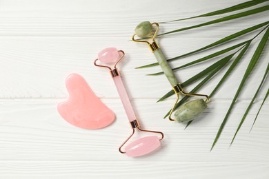 Photo of Face rollers, gua sha tool and leaf on white wooden background, flat lay