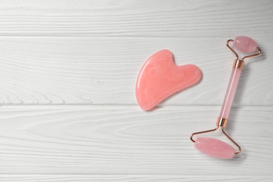 Photo of Face roller and gua sha tool on white wooden background, top view. Space for text