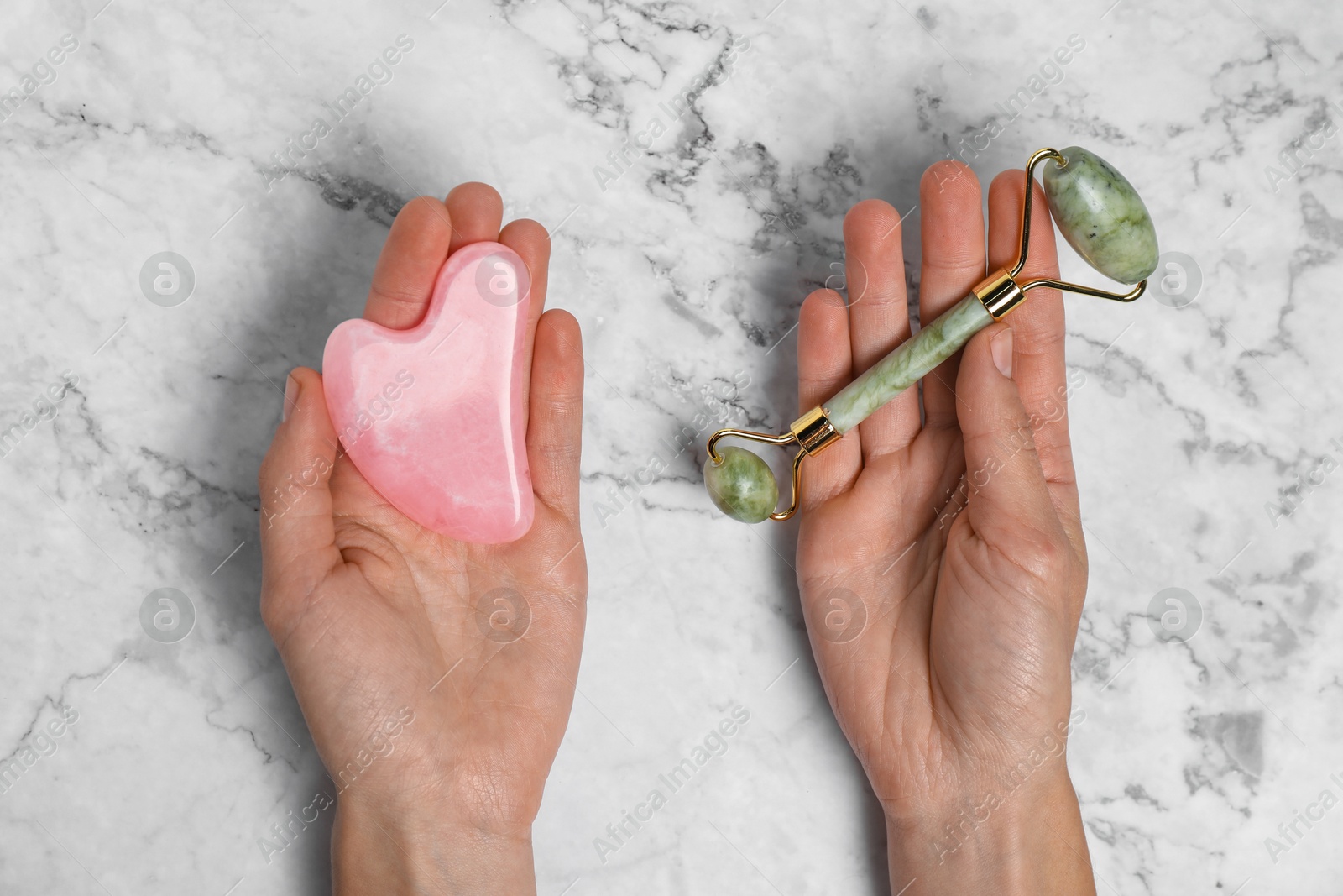 Photo of Woman with face roller and gua sha tool on white marble background, top view