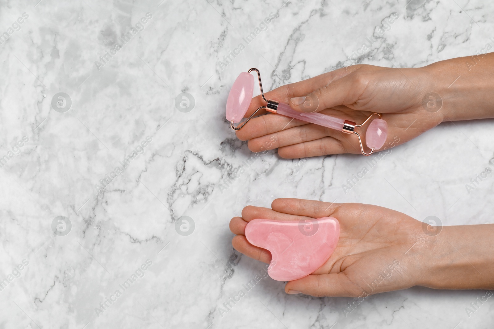 Photo of Woman with face roller and gua sha tool on white marble background, above view. Space for text