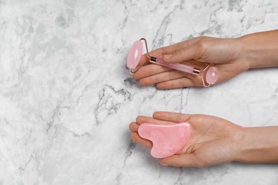 Photo of Woman with face roller and gua sha tool on white marble background, above view. Space for text