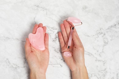 Photo of Woman with face roller and gua sha tool on white marble background, above view