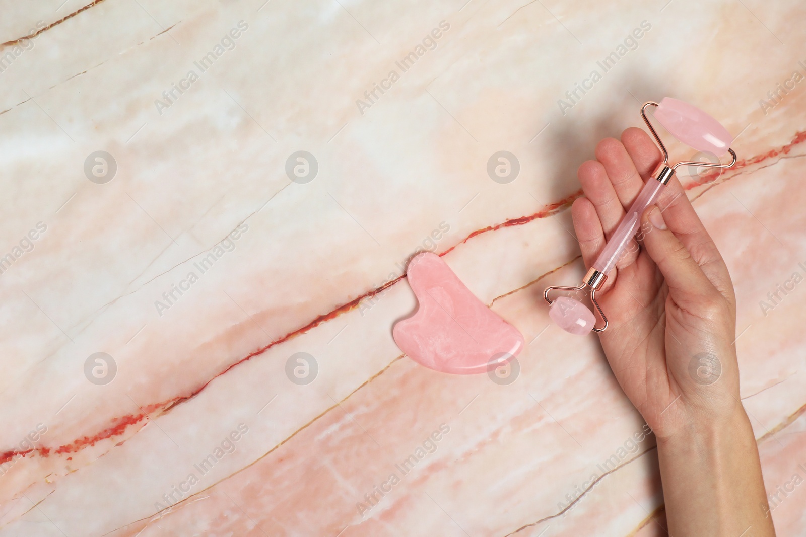 Photo of Woman with face roller and gua sha tool on pink marble background, top view. Space for text