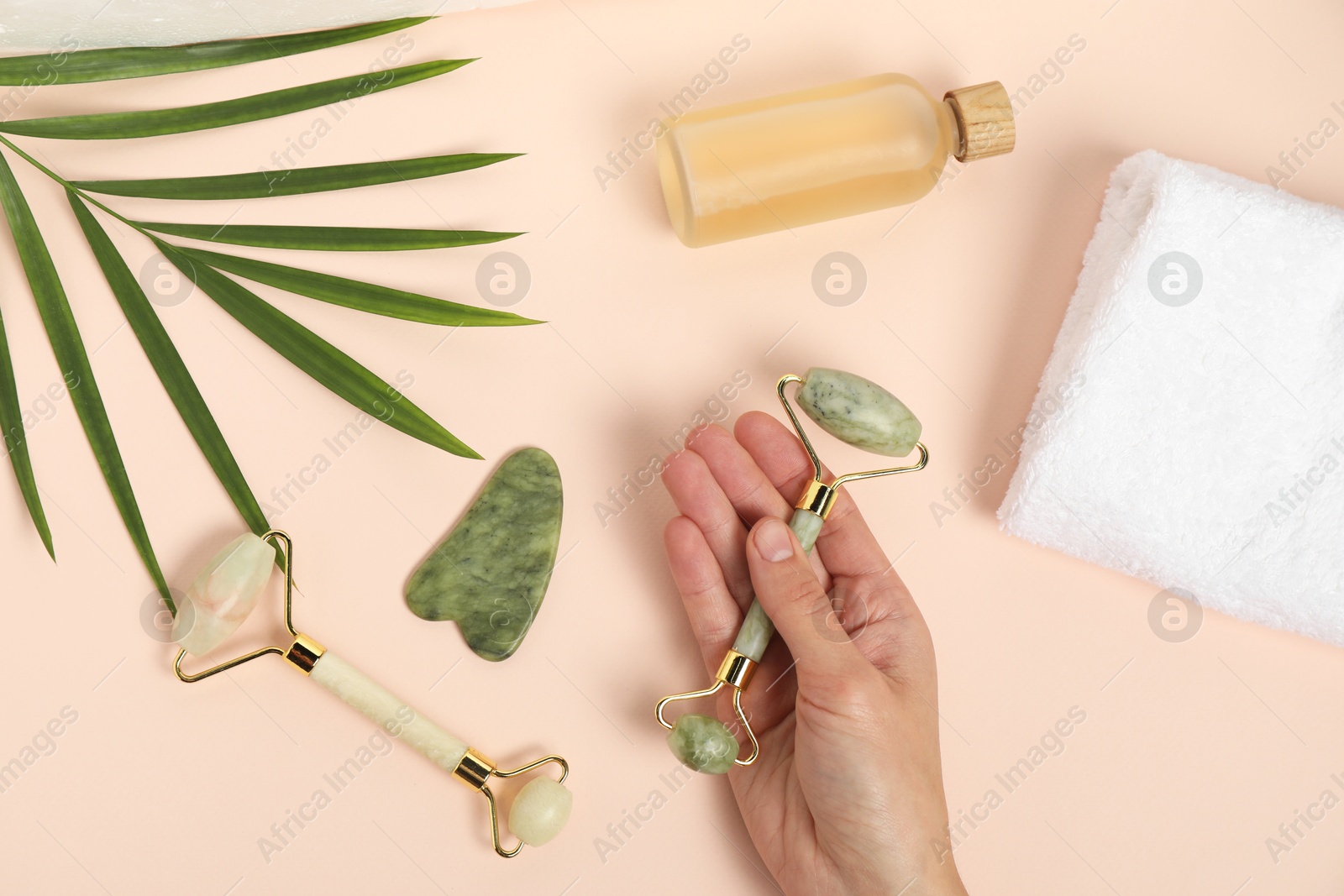 Photo of Woman with face rollers, gua sha tool, cosmetic product, towel and leaf on beige background, top view