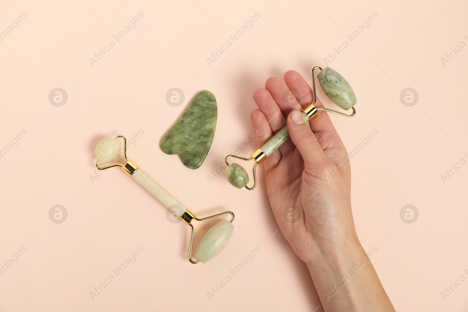 Photo of Woman with face rollers and gua sha tool on beige background, top view