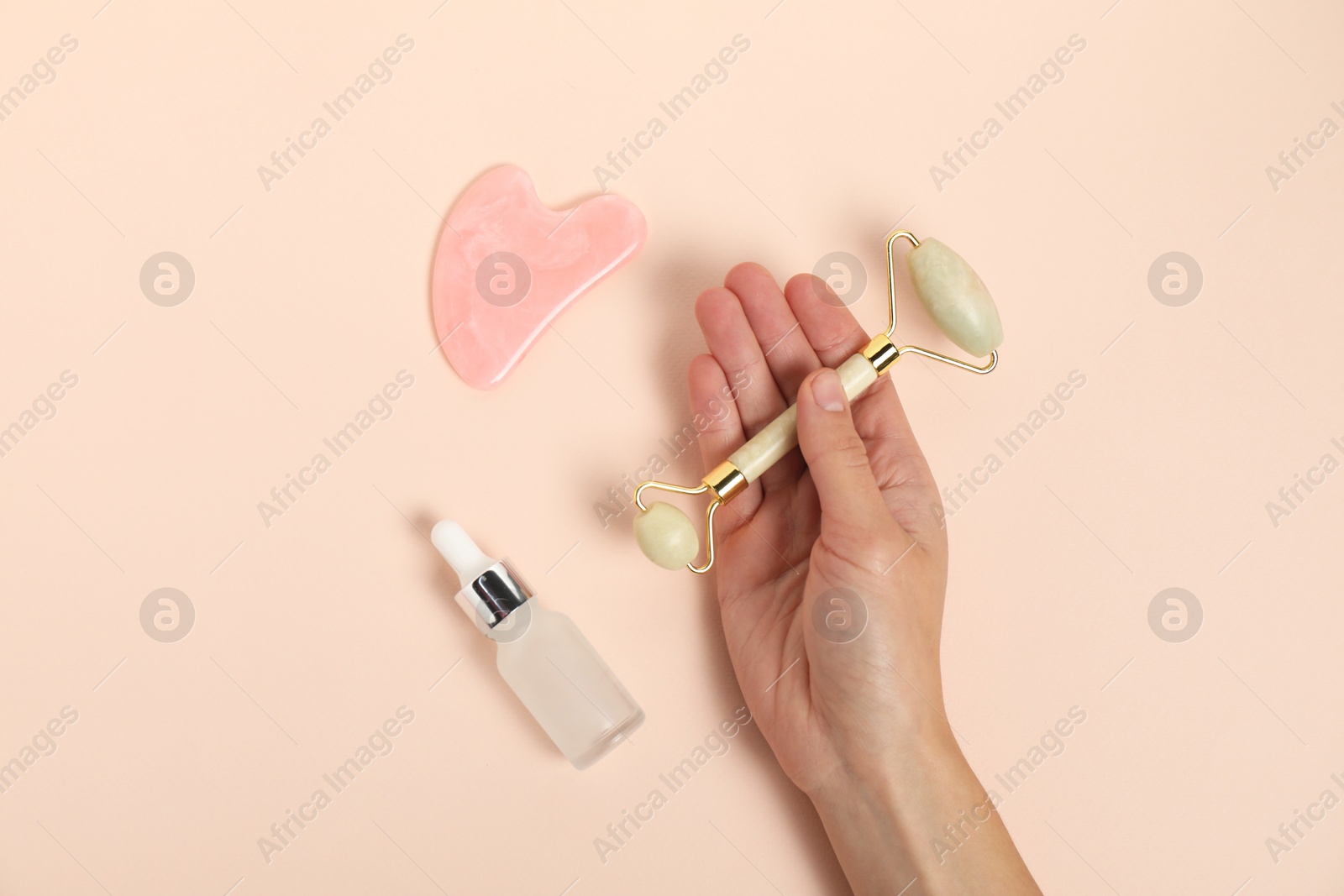 Photo of Woman with face roller, gua sha tool and cosmetic product on beige background, top view