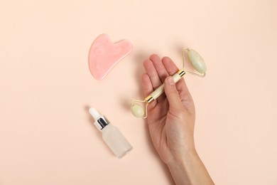 Photo of Woman with face roller, gua sha tool and cosmetic product on beige background, top view