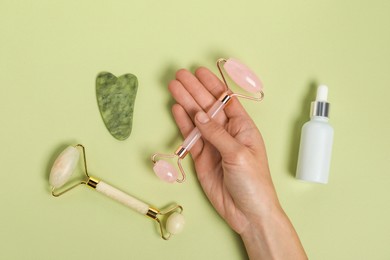 Photo of Woman with face rollers, gua sha tool and cosmetic product on light green background, top view