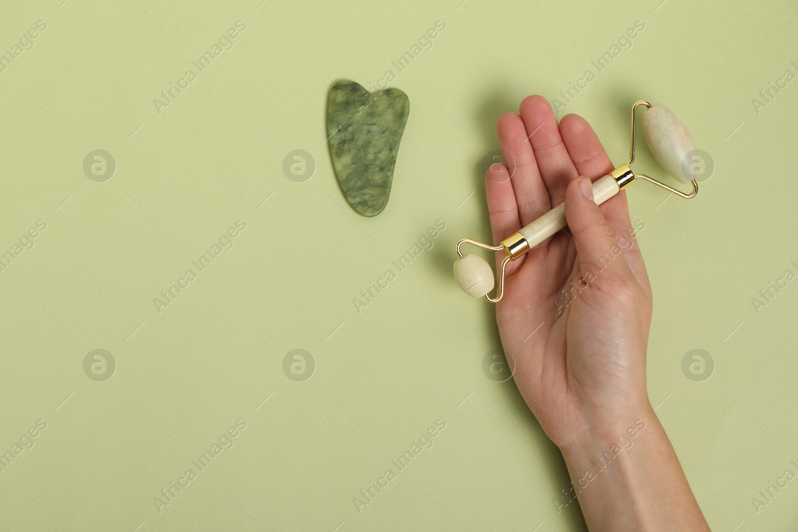 Photo of Woman with face roller and gua sha tool on light green background, top view. Space for text