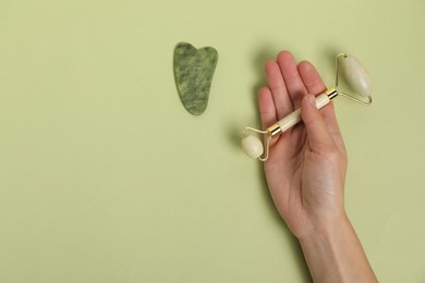 Photo of Woman with face roller and gua sha tool on light green background, top view. Space for text