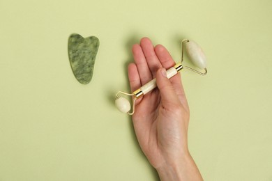 Photo of Woman with face roller and gua sha tool on light green background, top view