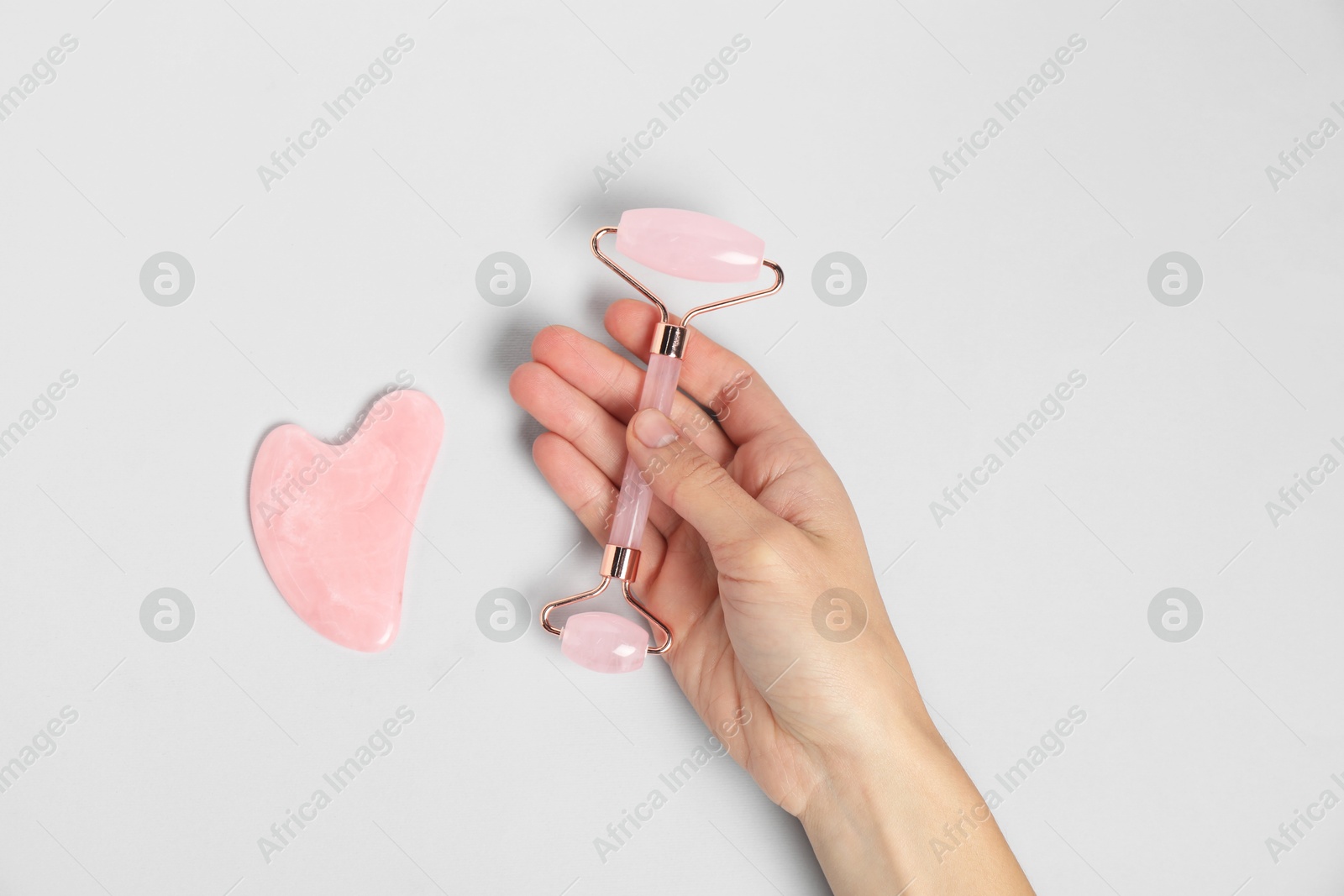 Photo of Woman with face roller and gua sha tool on light background, top view