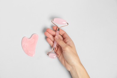 Photo of Woman with face roller and gua sha tool on light background, top view