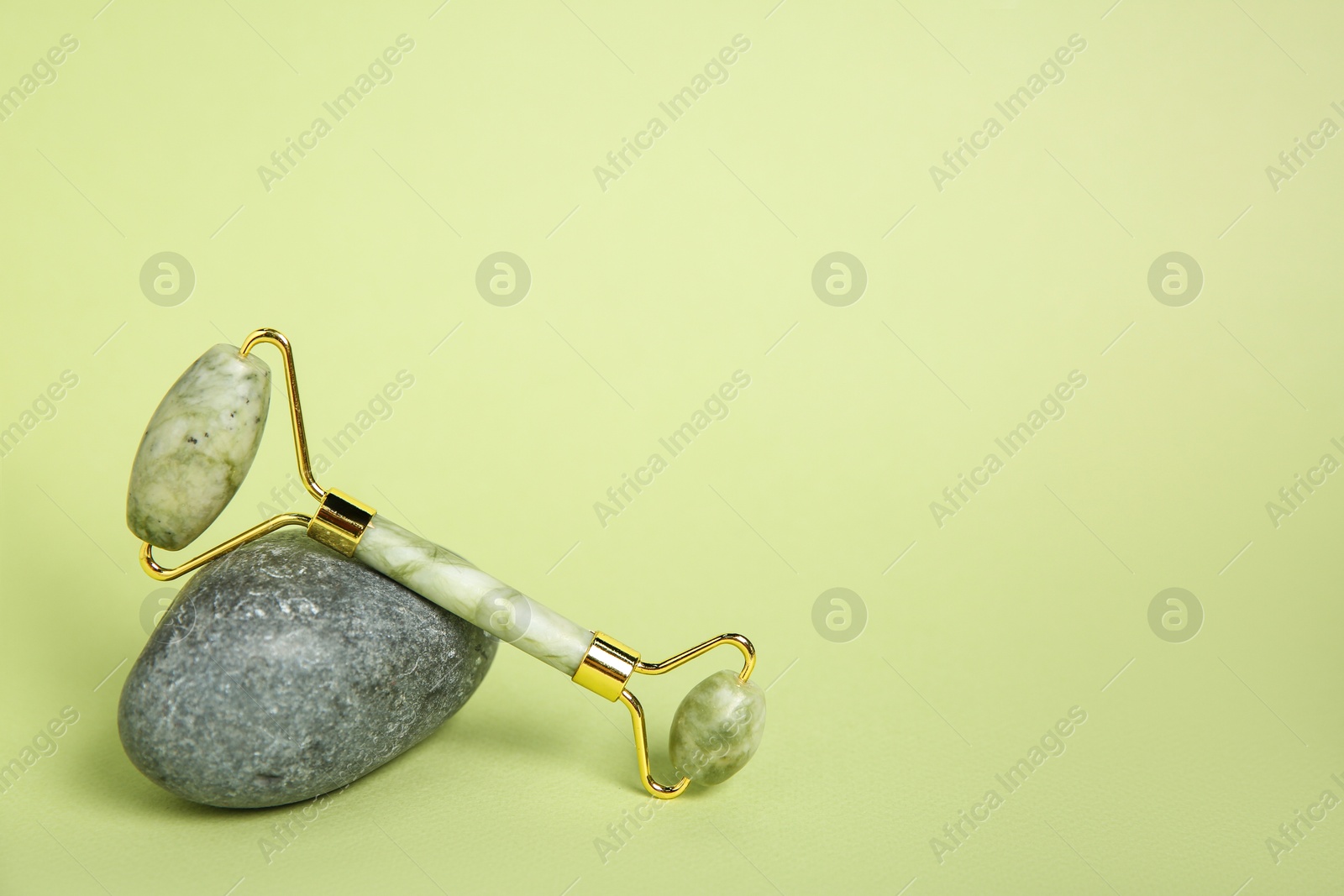 Photo of Face roller and stone on light green background. Space for text