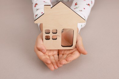 Photo of Adoption. Little girl with house figure at beige table, closeup