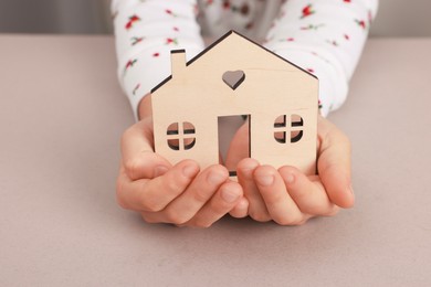 Photo of Adoption. Little girl with house figure at beige table, closeup