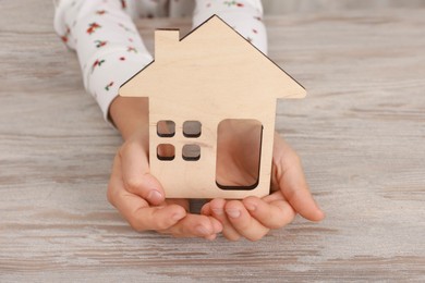 Photo of Adoption. Little girl with house figure at wooden table, closeup