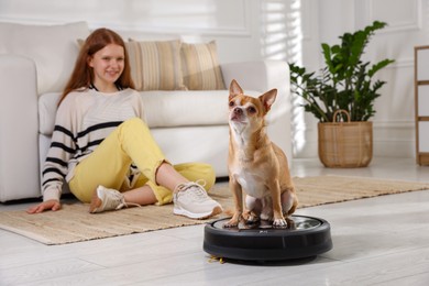 Photo of Teenage girl and her cute Chihuahua dog on robotic vacuum cleaner at home, selective focus