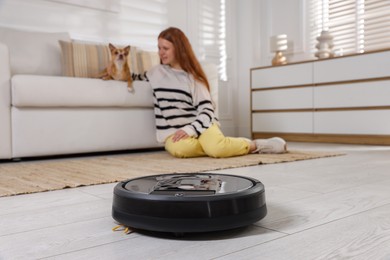 Photo of Teenage girl and her cute Chihuahua dog at home, focus on robotic vacuum cleaner