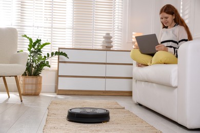 Photo of Teenage girl with laptop at home, focus on robotic vacuum cleaner