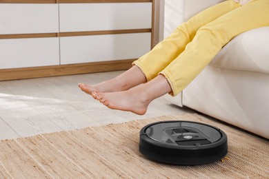 Photo of Teenage girl sitting on sofa while robotic vacuum cleaner vacuuming rug at home, closeup