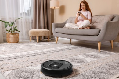 Photo of Teenage girl with smartphone at home, focus on robotic vacuum cleaner