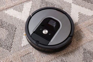 Photo of Robotic vacuum cleaner vacuuming rug indoors, above view