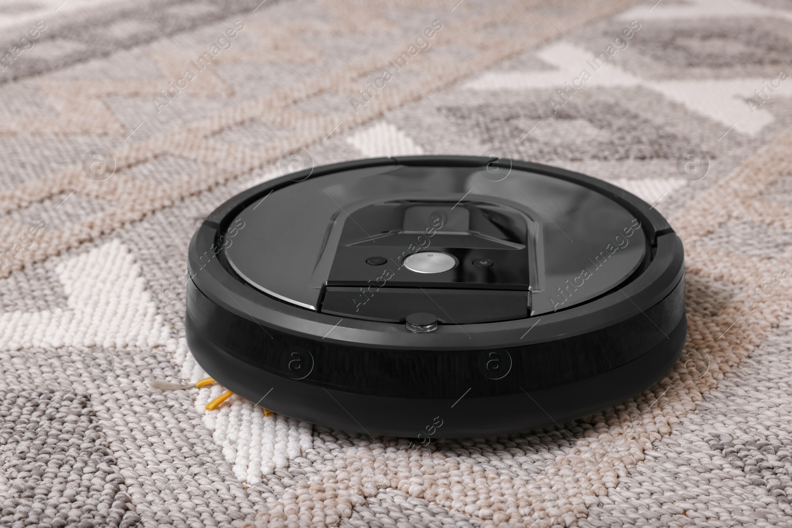 Photo of Modern robotic vacuum cleaner vacuuming rug at home, closeup