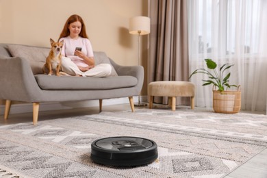 Photo of Teenage girl with smartphone and her cute Chihuahua dog at home, focus on robotic vacuum cleaner