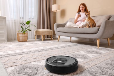 Teenage girl with smartphone and her cute Chihuahua dog at home, focus on robotic vacuum cleaner