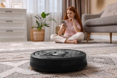 Photo of Teenage girl with smartphone at home, focus on robotic vacuum cleaner