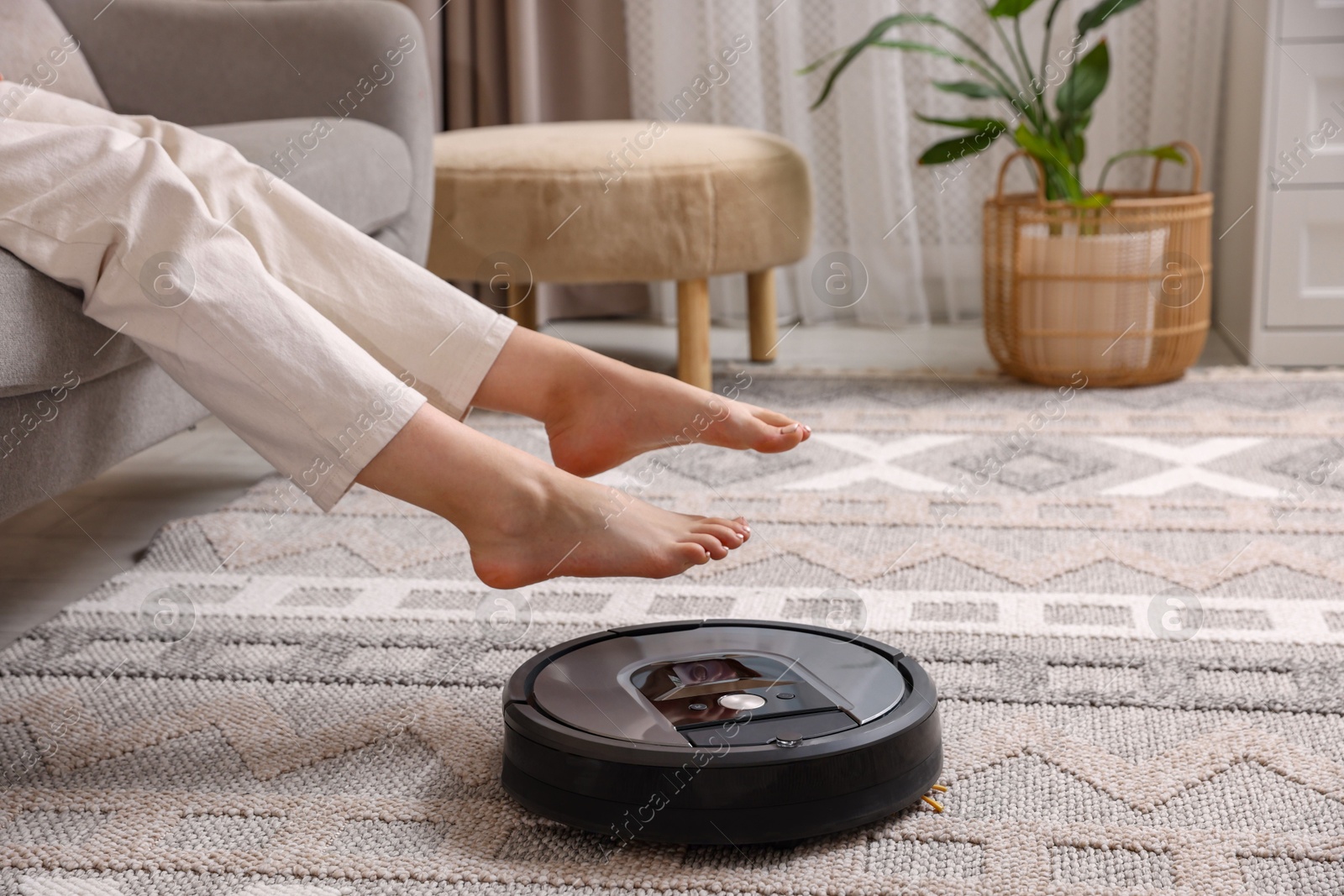 Photo of Teenage girl sitting on sofa while robotic vacuum cleaner vacuuming rug at home, closeup