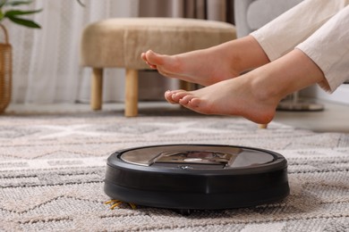 Photo of Teenage girl sitting on sofa while robotic vacuum cleaner vacuuming rug at home, closeup