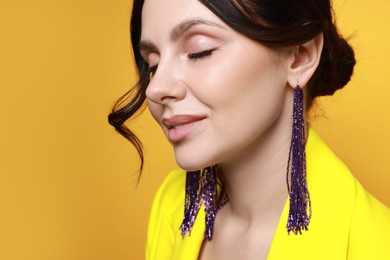 Photo of Beautiful young woman wearing stylish earrings on orange background, closeup