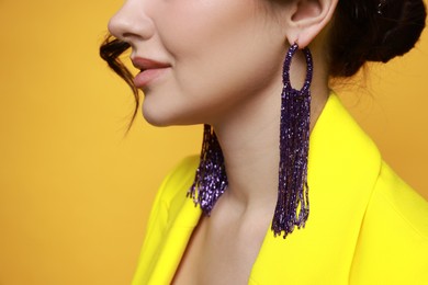 Photo of Woman wearing stylish earrings on orange background, closeup