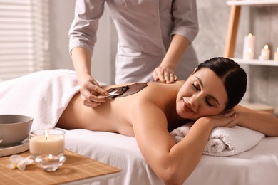 Photo of Chocolate body wrap. Spa worker applying mask onto woman's back in salon, closeup