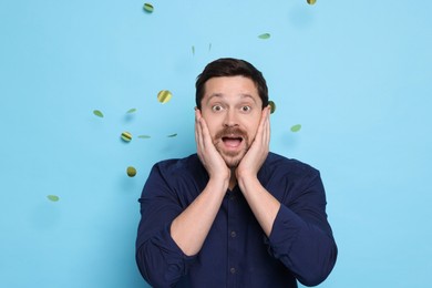 Photo of Emotional man and flying confetti on light blue background. Surprise party