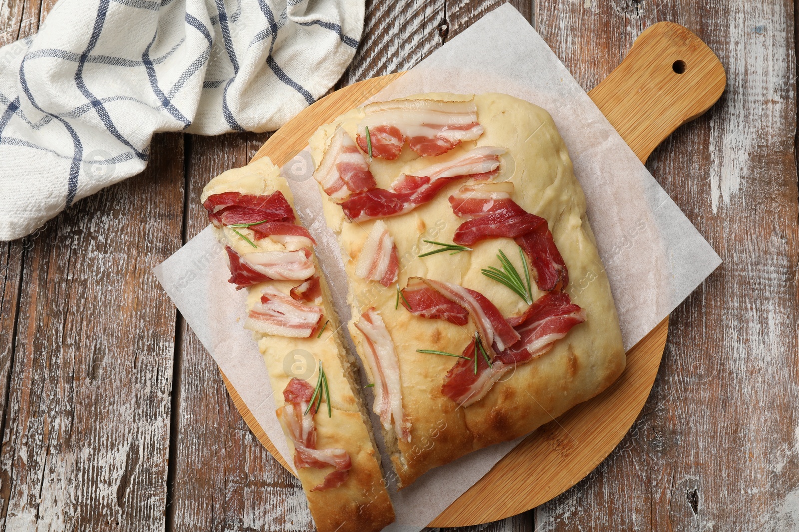 Photo of Pieces of delicious focaccia bread with bacon and rosemary on wooden table, top view