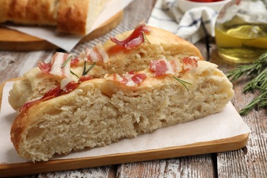 Photo of Slices of delicious focaccia bread with bacon and rosemary on wooden table, closeup