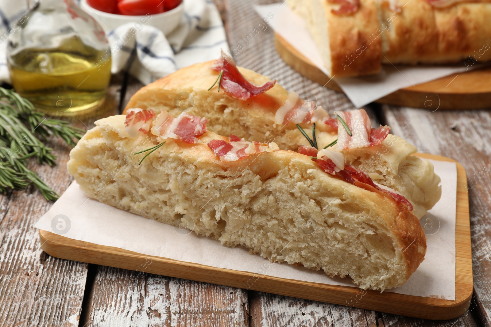 Photo of Slices of delicious focaccia bread with bacon and rosemary on wooden table, closeup