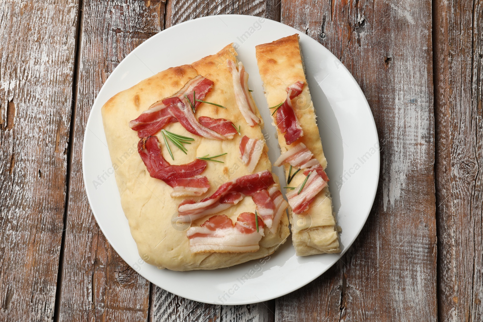 Photo of Pieces of delicious focaccia bread with bacon and rosemary on wooden table, top view