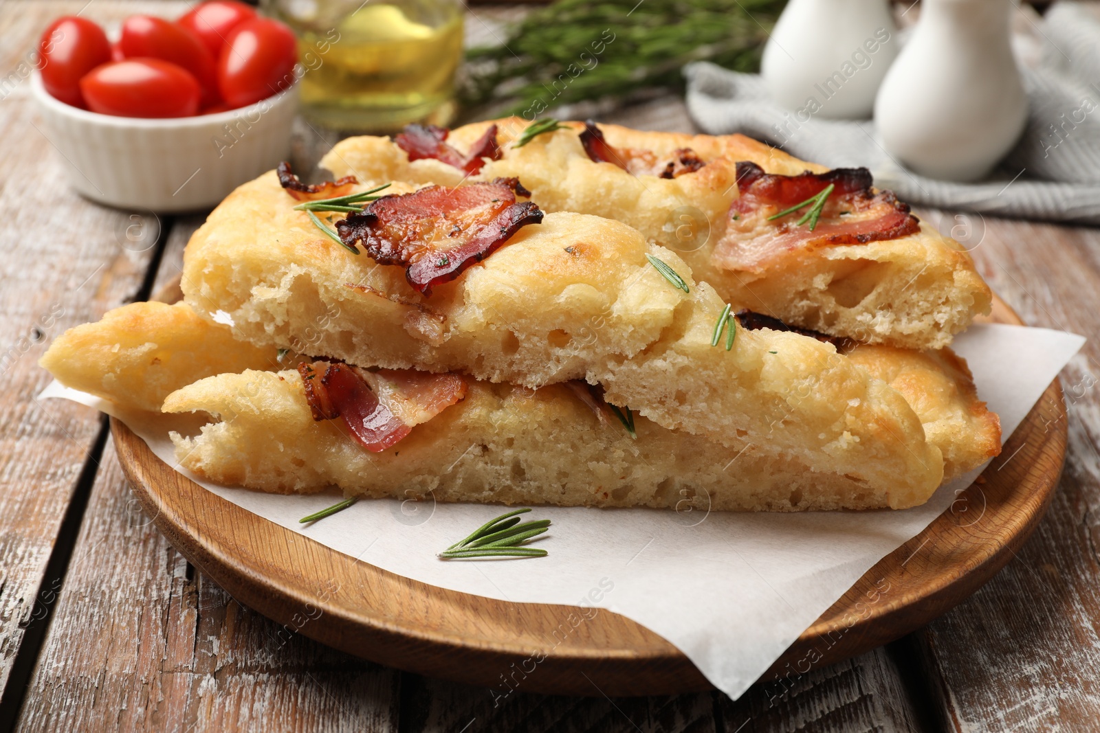 Photo of Slices of delicious focaccia bread with bacon, rosemary and tomatoes on wooden table, closeup