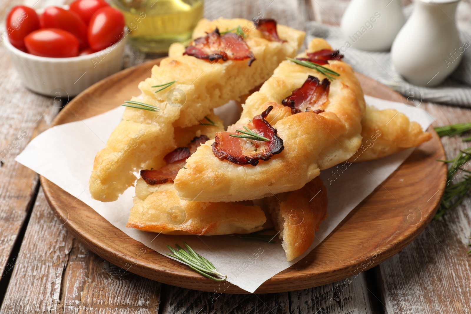 Photo of Slices of delicious focaccia bread with bacon, rosemary and tomatoes on wooden table, closeup