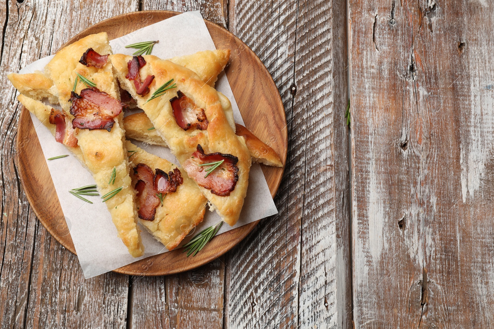 Photo of Slices of delicious focaccia bread with bacon and rosemary on wooden table, top view. Space for text