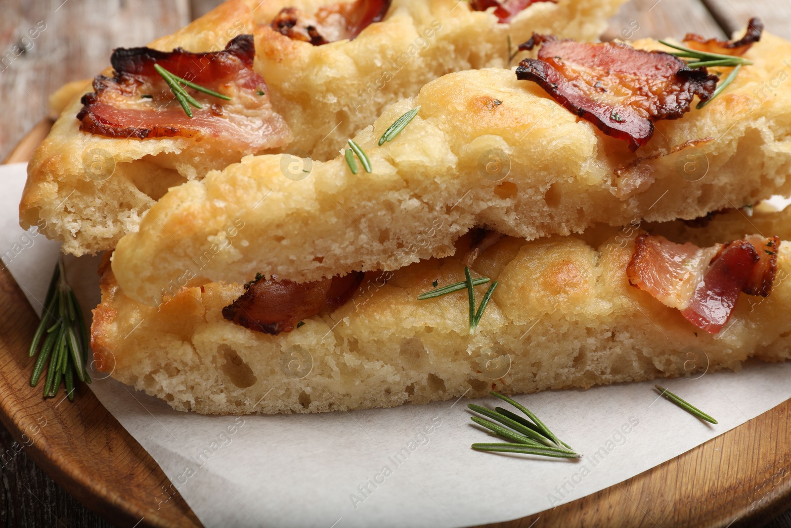 Photo of Slices of delicious focaccia bread with bacon and rosemary on table, closeup