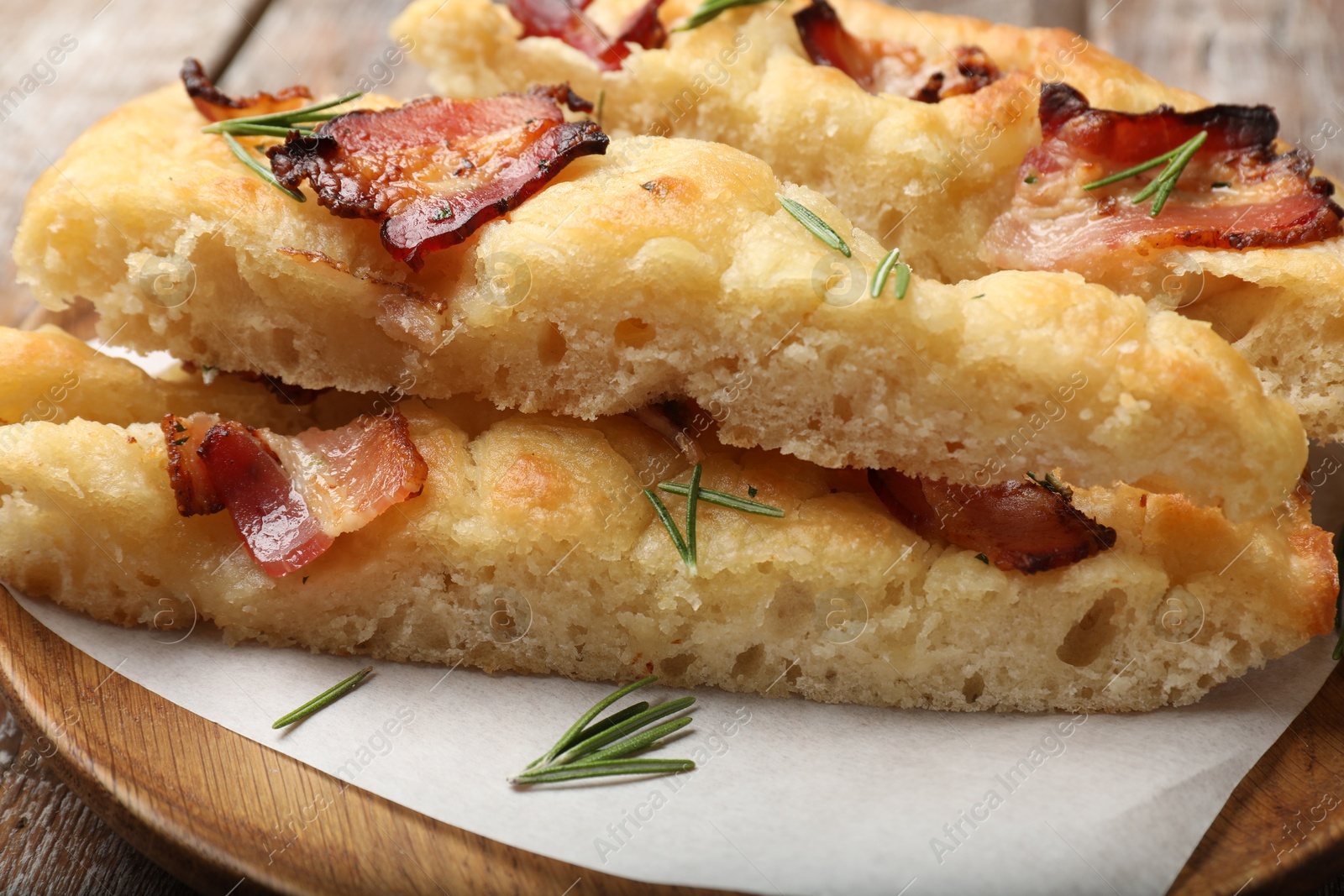 Photo of Slices of delicious focaccia bread with bacon and rosemary on table, closeup