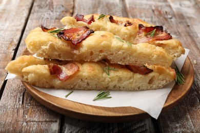 Photo of Slices of delicious focaccia bread with bacon and rosemary on wooden table, closeup