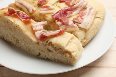 Photo of Pieces of delicious focaccia bread with bacon and rosemary on wooden table, closeup