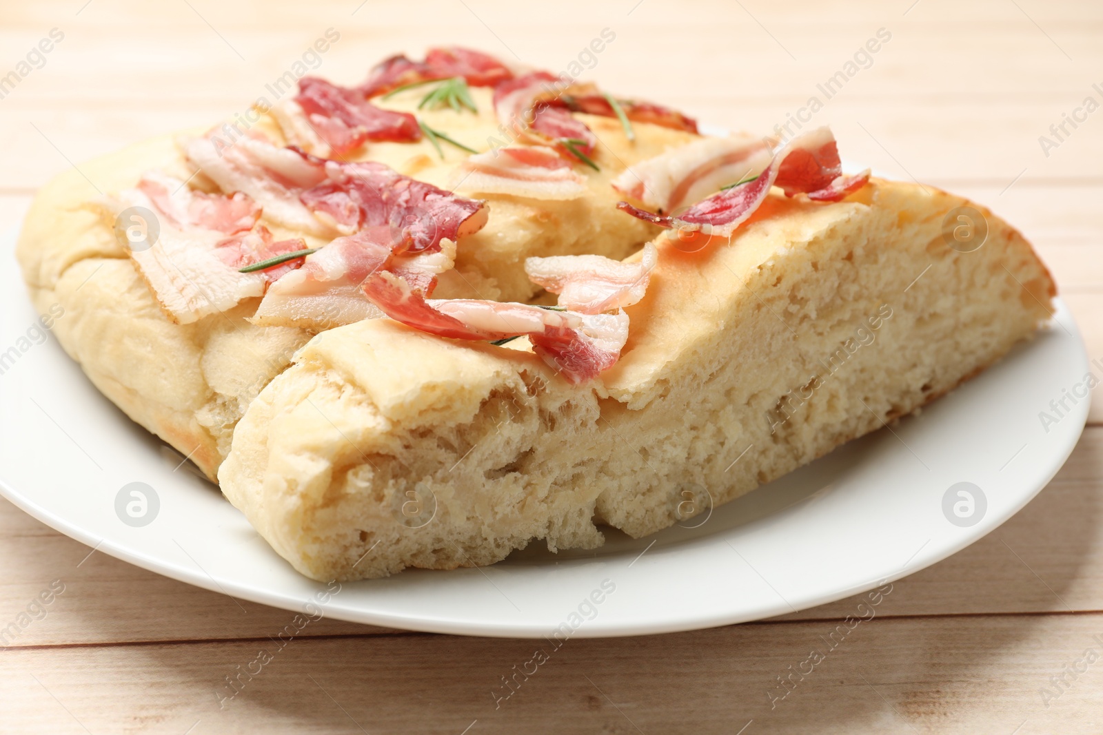 Photo of Pieces of delicious focaccia bread with bacon and rosemary on wooden table, closeup