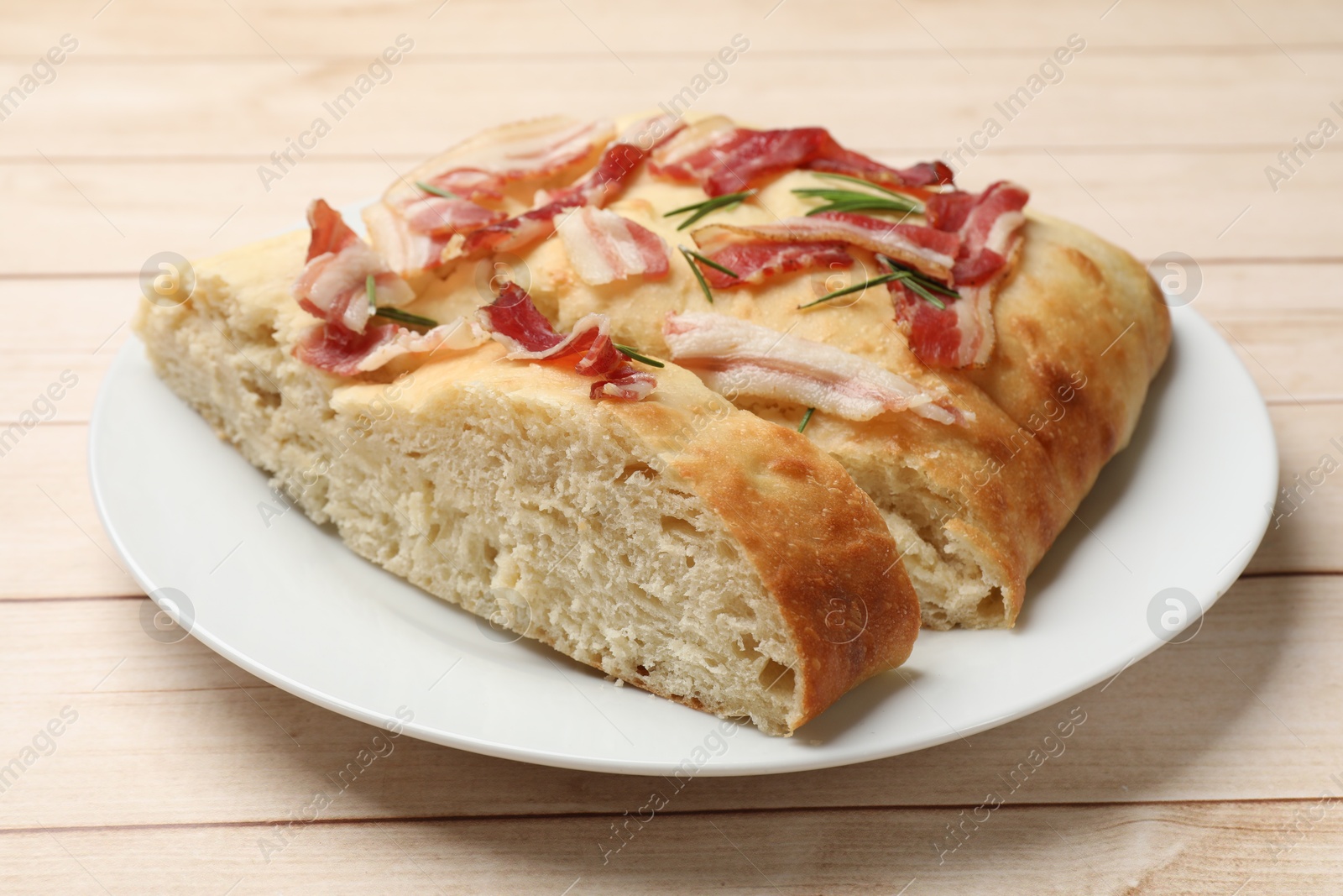 Photo of Pieces of delicious focaccia bread with bacon and rosemary on wooden table, closeup